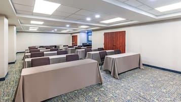 A conference room with rows of tables and chairs, a carpeted floor, and a wooden door.