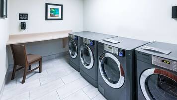 A laundry room with three front-loading washing machines, a chair, and a small table.