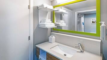Un baño moderno con un lavamanos blanco, un espejo con marco verde y toallas ordenadas en un estante.