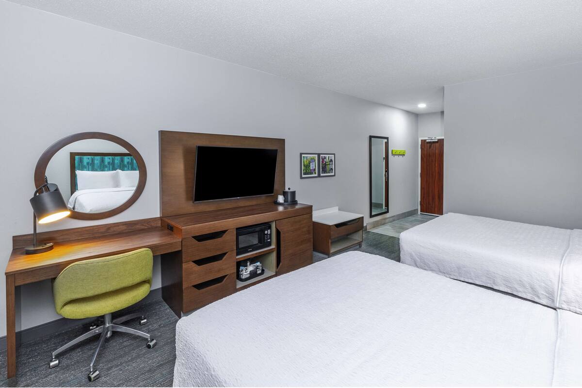 A hotel room with a bed, a desk with a computer, a TV, a mirror, and a small bathroom.