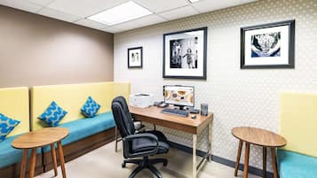 A modern office space with a desk, computer, and office chair. There is a sofa with blue cushions and a small round table.