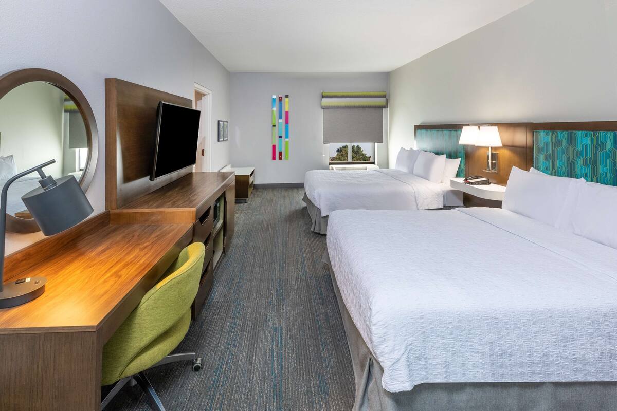 A hotel room with a desk, two beds, a TV, and a window with a view.