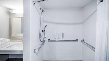 Un baño moderno con cabina de ducha, barras de apoyo, lavamanos y espejo.