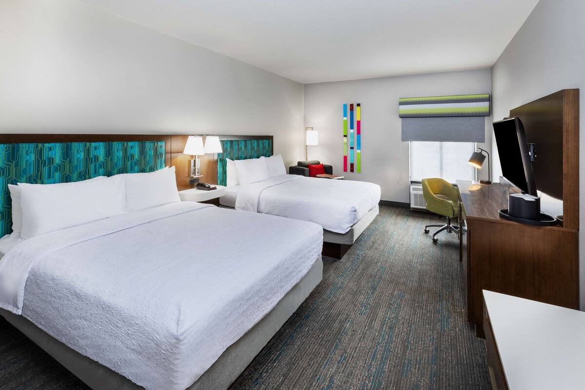A hotel room with two beds, a desk, a chair, and a television.