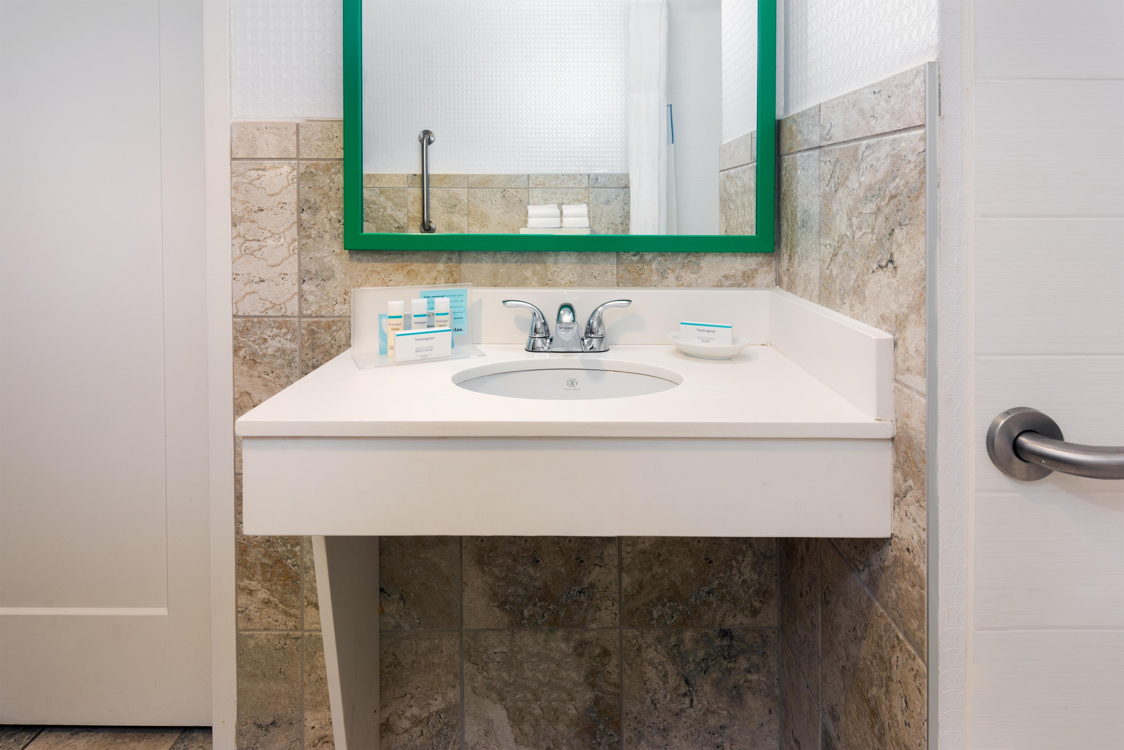 Un baño con un lavamanos blanco, un espejo con marco verde y artículos de aseo en el mostrador.