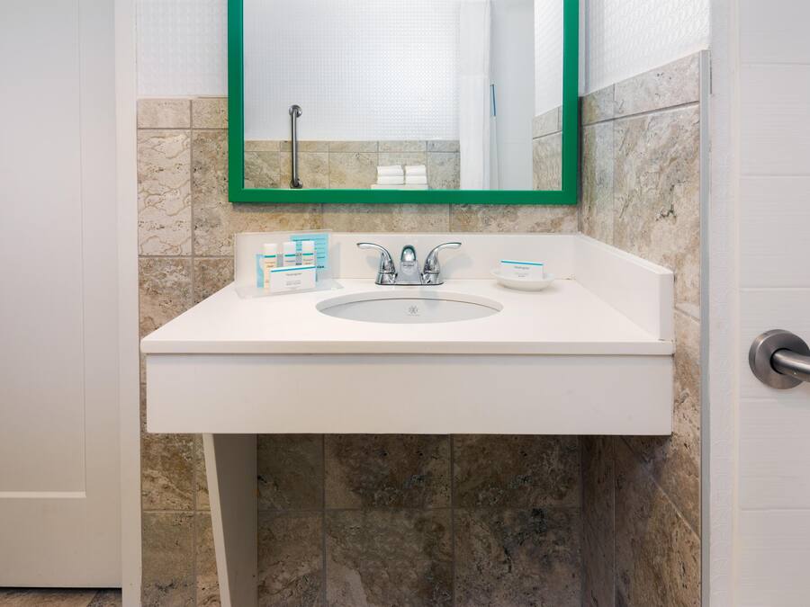 Un baño con un lavamanos blanco, un espejo con marco verde y artículos de aseo en el mostrador.
