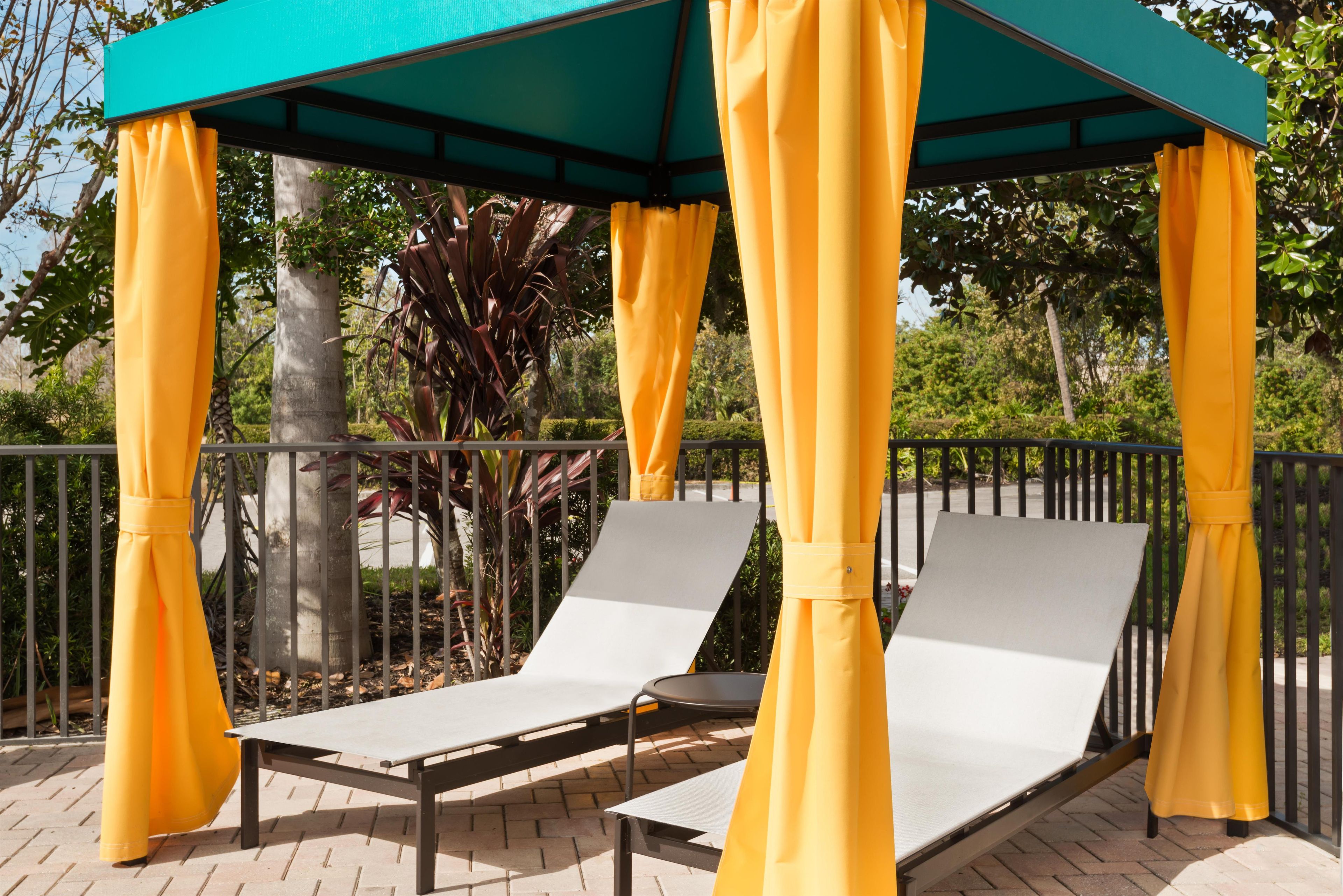 A covered outdoor seating area with two lounge chairs and yellow curtains.