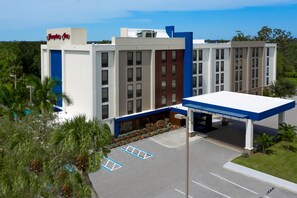 A hotel with a modern design, featuring a prominent entrance with a blue canopy, a parking lot with marked spaces, and a surrounding landscape with palm trees. - Hampton Inn Ellenton/Bradenton (Ellenton)
