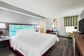 Een hotelkamer met een groot bed, nachtkastjes, een bureau met stoel, een televisie en een raam met zonwering.