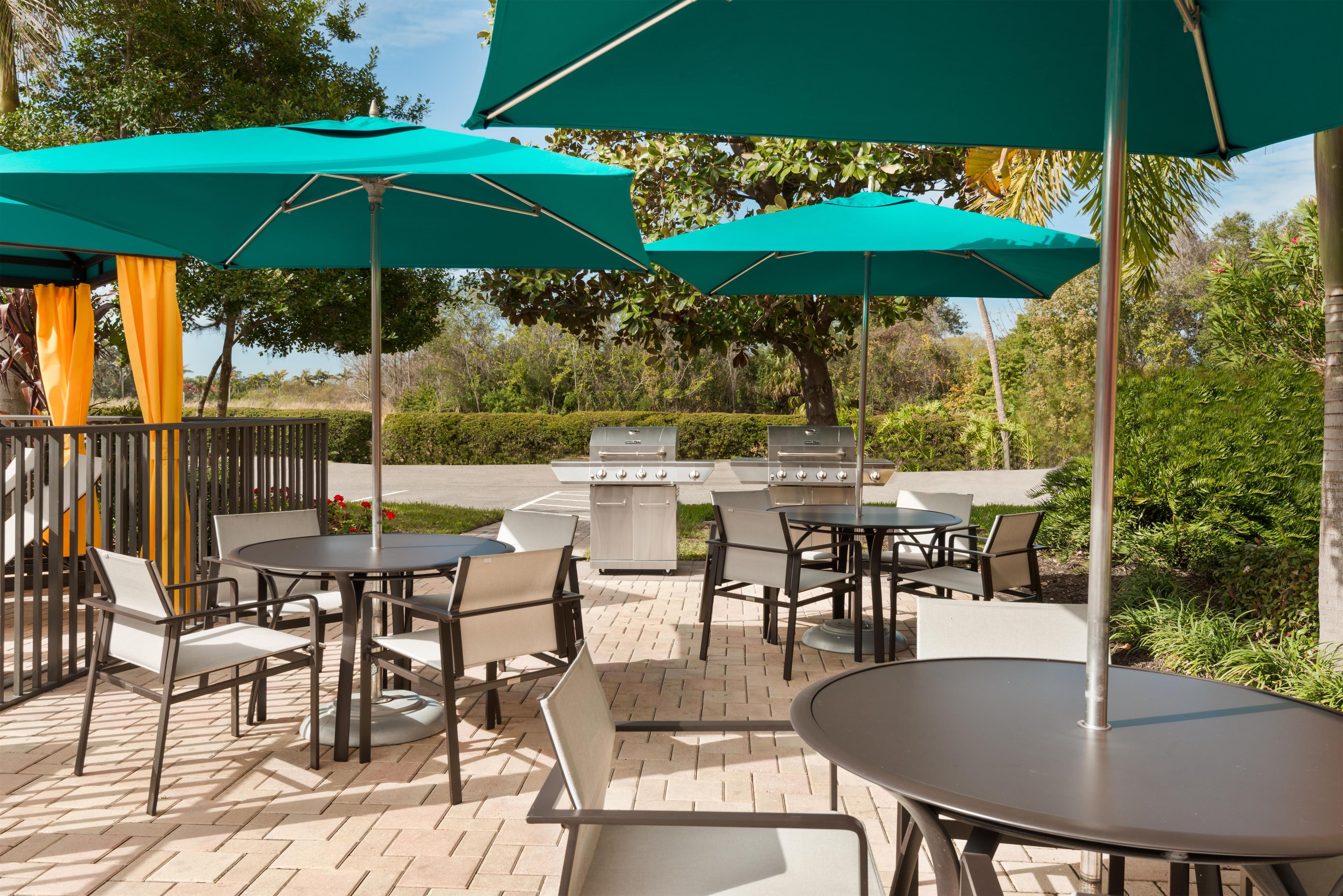 An outdoor patio area with tables and chairs, green umbrellas, and a barbecue grill.