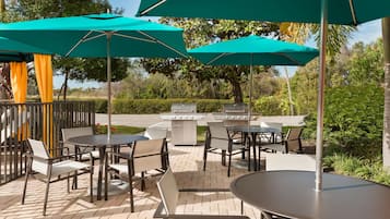 An outdoor patio area with tables and chairs, green umbrellas, and a barbecue grill.