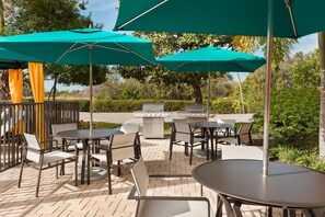 An outdoor patio area with tables and chairs, green umbrellas, and a barbecue grill. - Hampton Inn Ellenton/Bradenton (Ellenton)