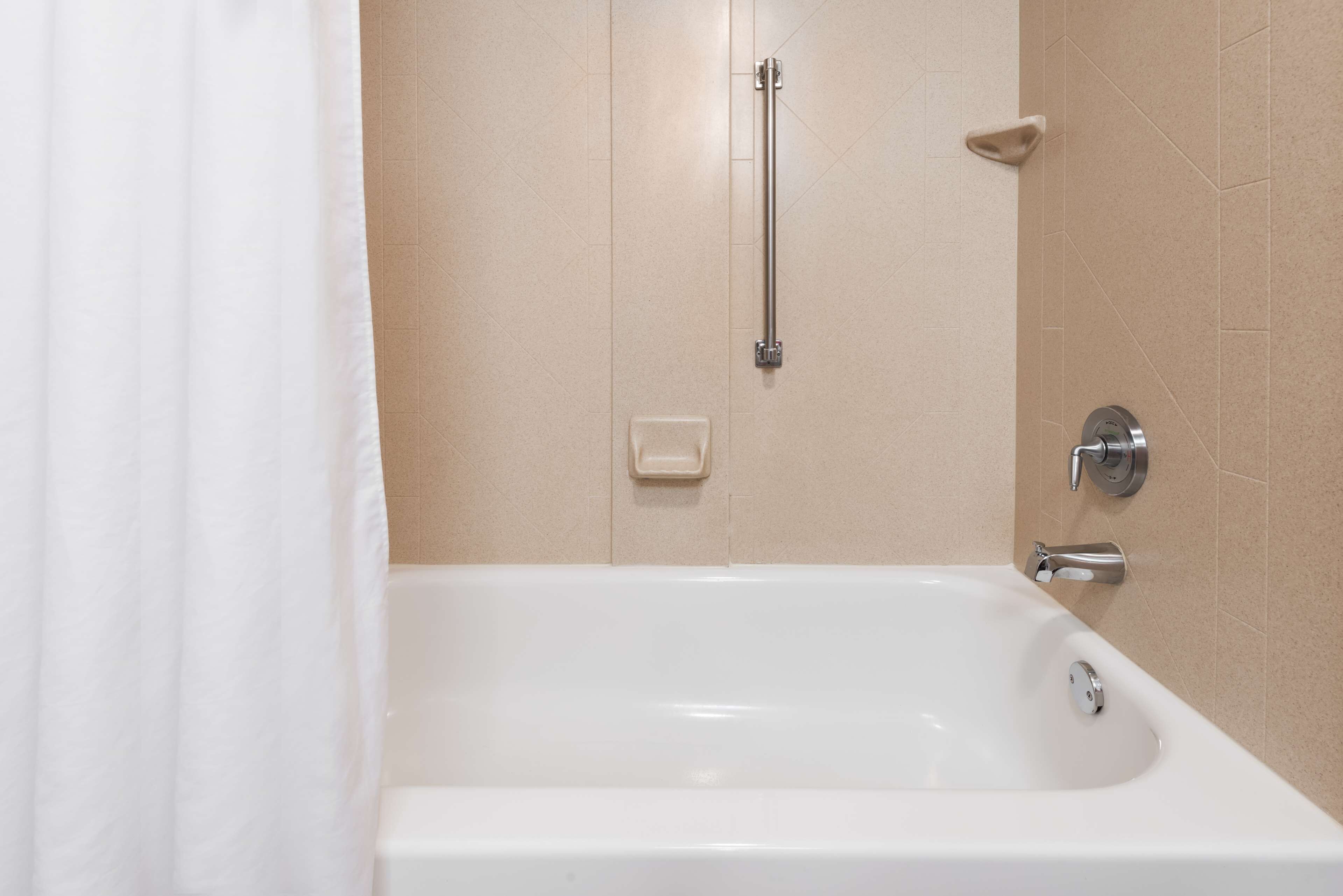 A white bathtub with a handheld showerhead, a towel rack, and a soap dish on beige tiled walls.