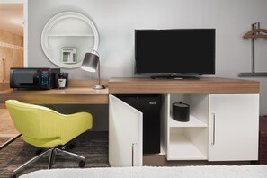 Een moderne hotelkamer met een flatscreen televisie, een magnetron, een koffiezetapparaat, een bureau met lamp, een stoel en een garderobe.
