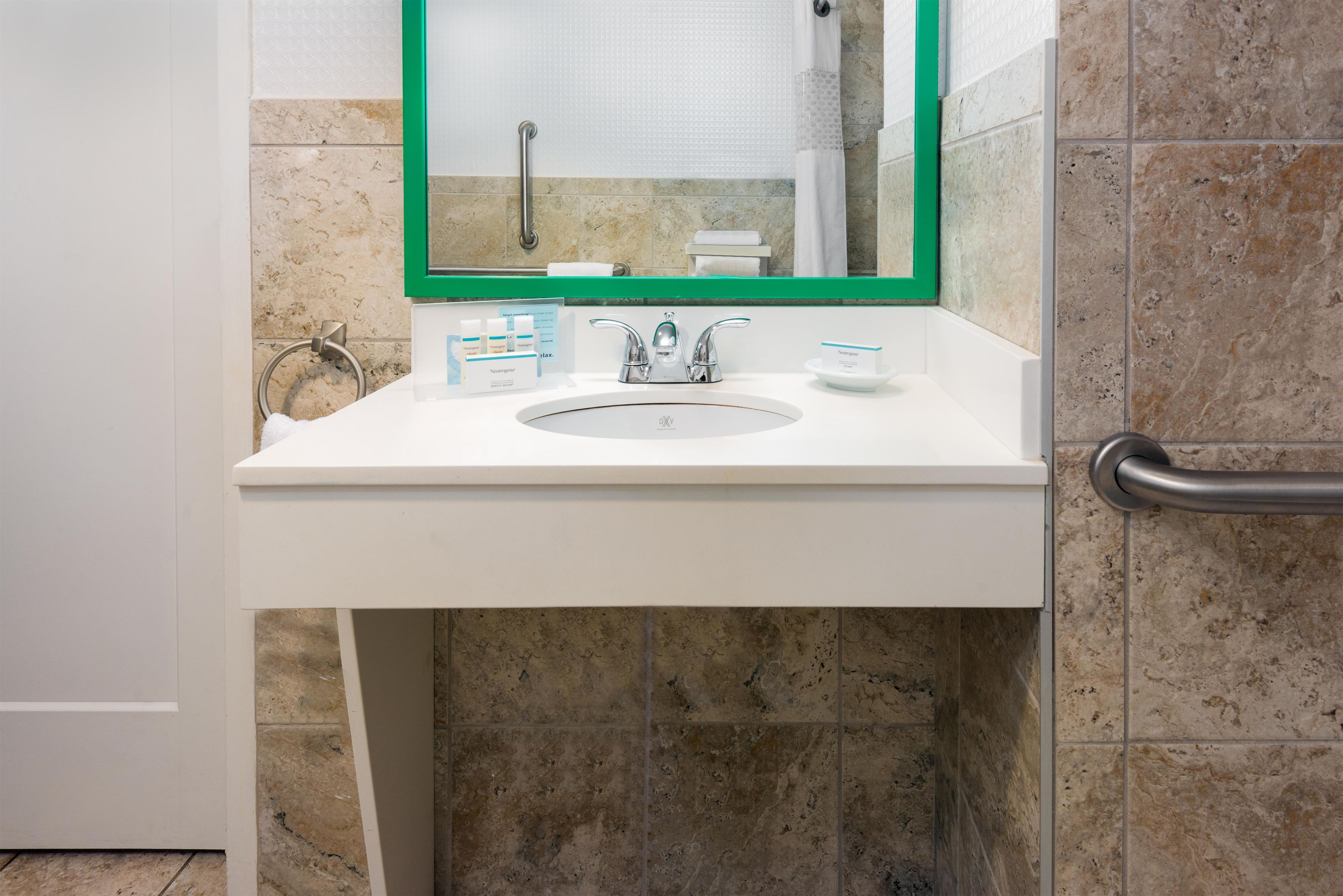 A bathroom with a white sink, a green-framed mirror, and a handrail.