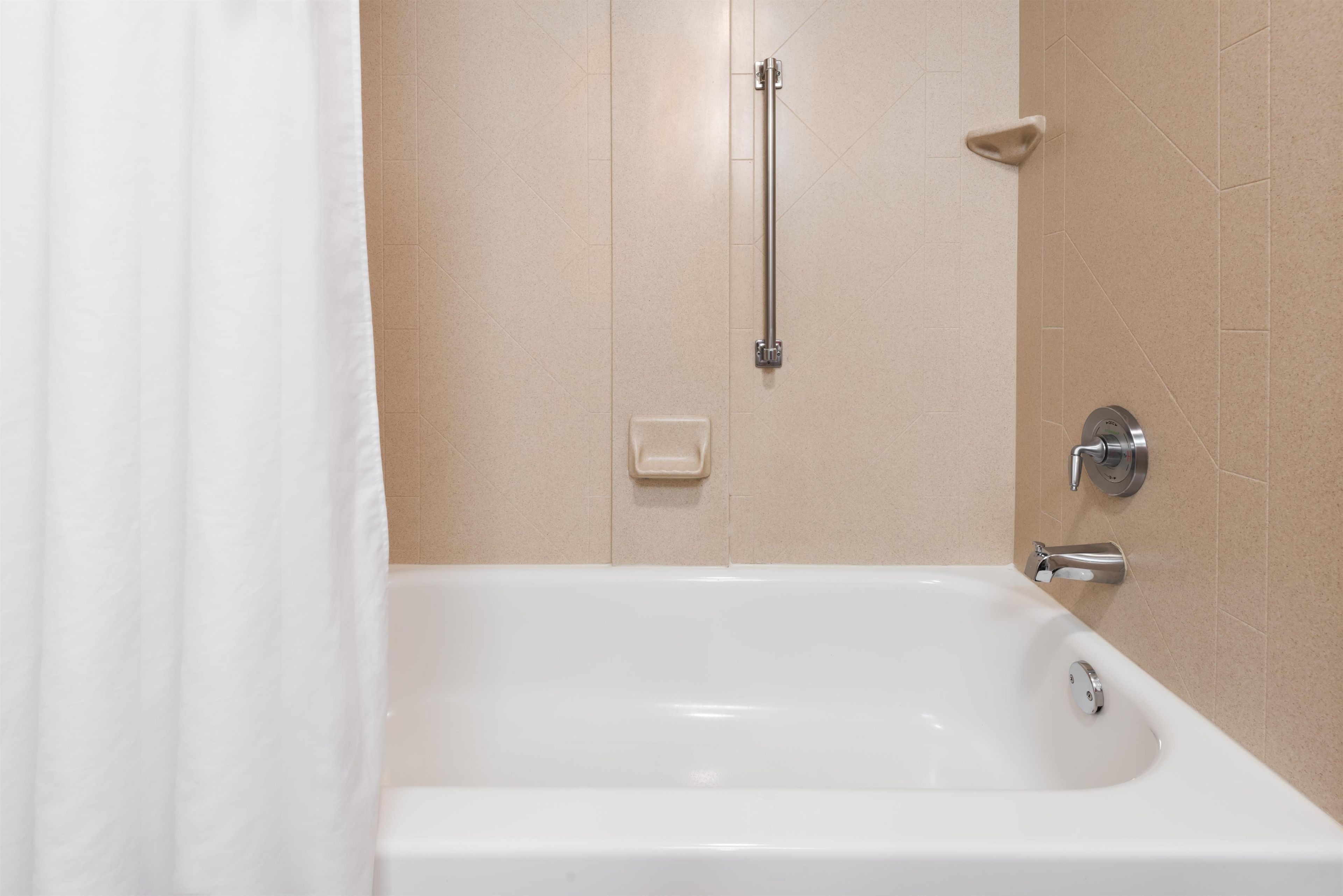 A white bathtub with a handheld showerhead, a wall-mounted faucet, and a corner grab bar.