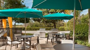 An outdoor patio with tables and chairs, green umbrellas, and a barbecue grill. - Hampton Inn Ellenton/Bradenton (Ellenton)
