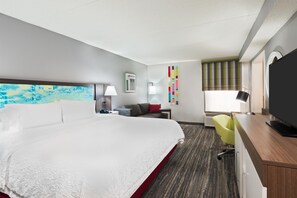 A hotel room with a large bed, a desk with a flat-screen TV, a chair, a desk lamp, and a window with blinds. - Hampton Inn Ellenton/Bradenton (Ellenton)