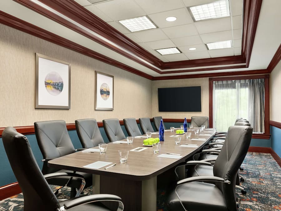 A conference room with a long table, multiple chairs, a large screen, and framed pictures on the wall.