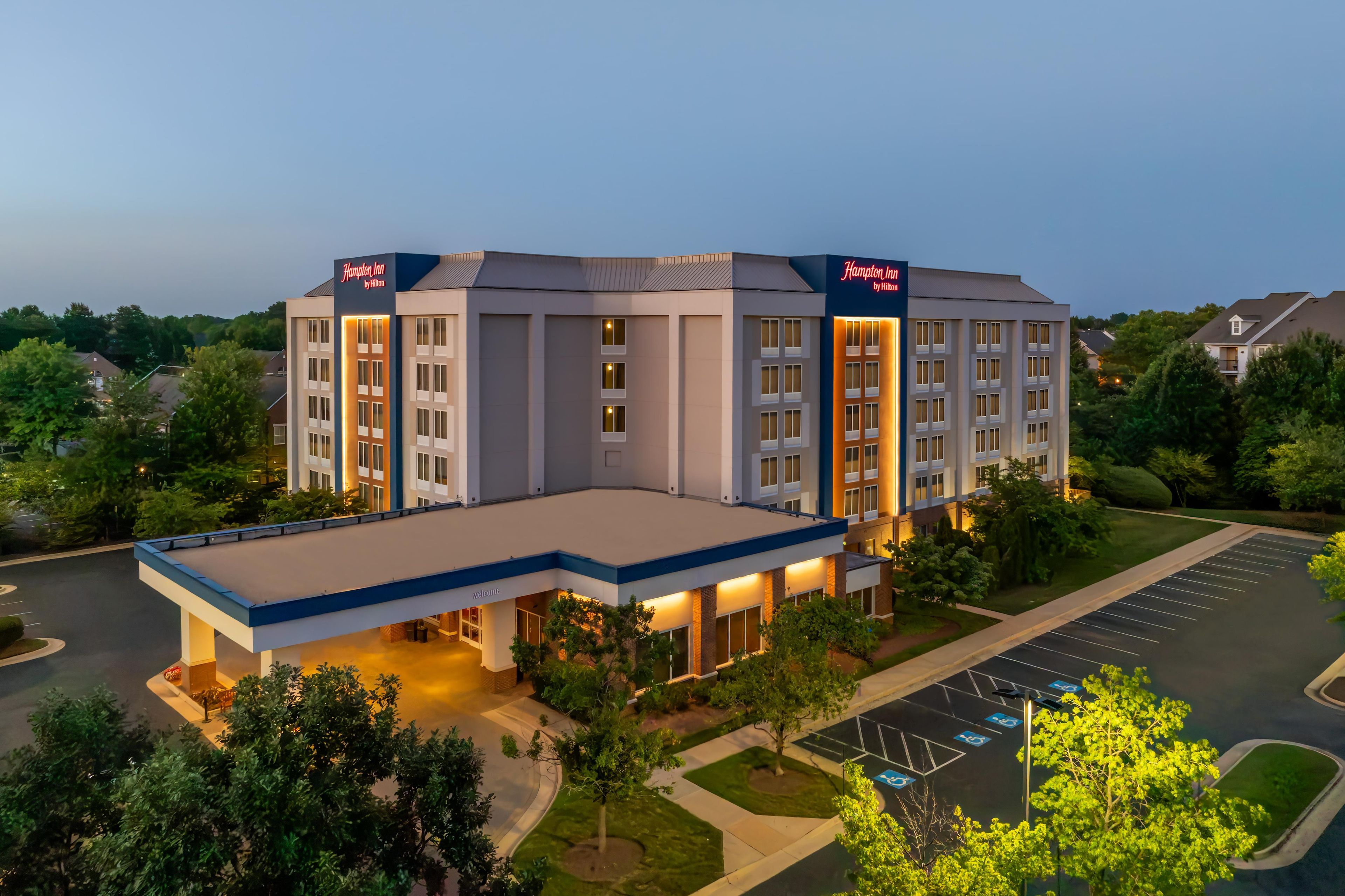 A Hampton Inn by Hilton hotel with a modern design, a parking lot, and a landscaped area.