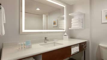 Un baño moderno con un espejo grande, lavabo blanco y toallas ordenadas.