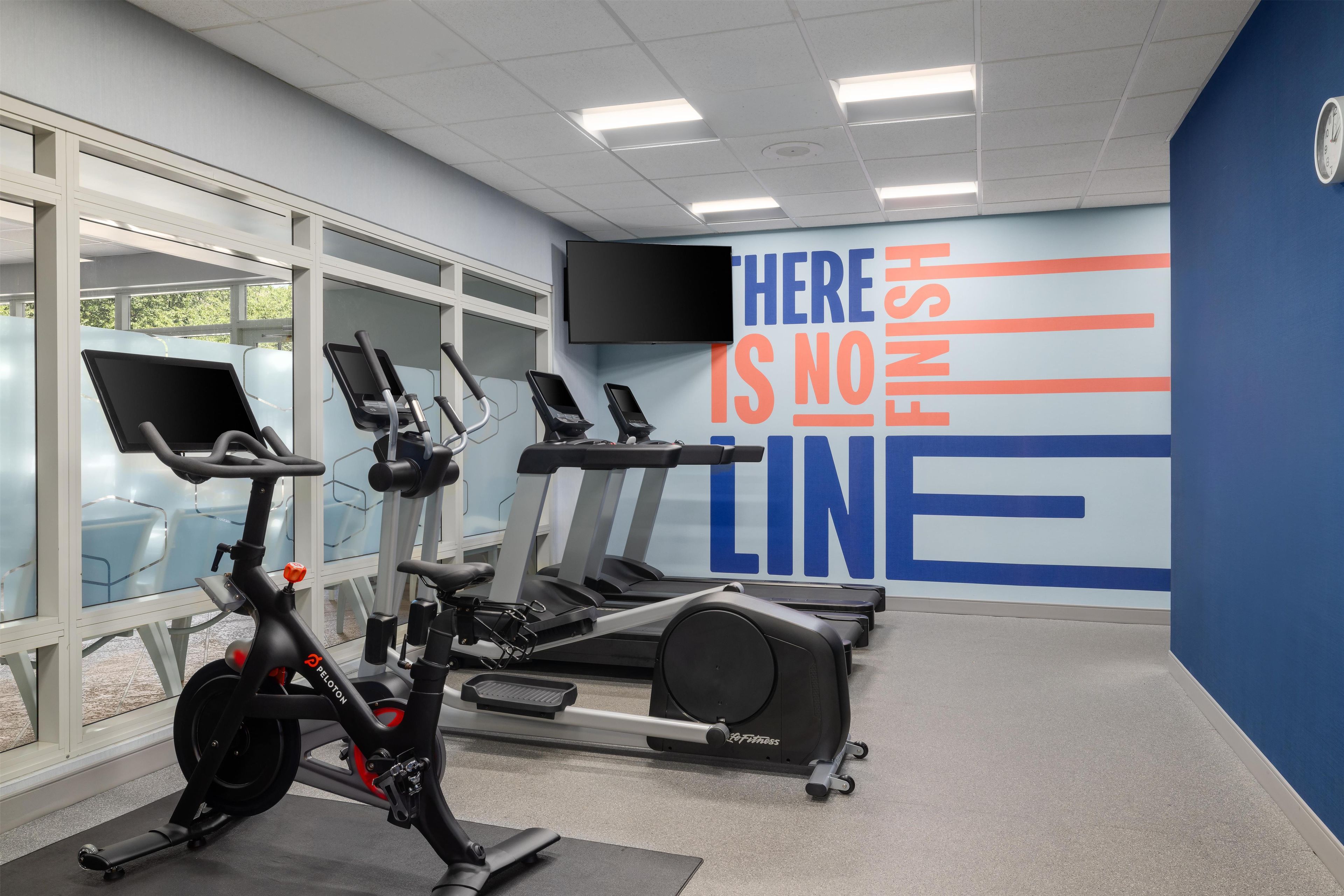 Un gimnasio con bicicletas estáticas, cintas de correr y una pared motivacional.