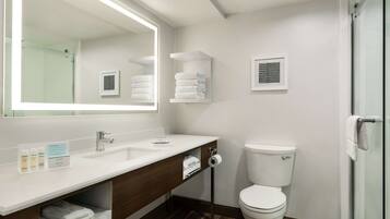 A modern bathroom with a white sink, mirror, and toilet. There are towels and toiletries on the counter.
