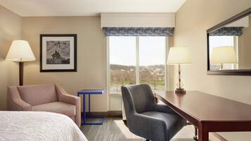 Una habitación de hotel con una cama, dos sillones, un escritorio, una ventana con vistas y un cuadro en la pared.