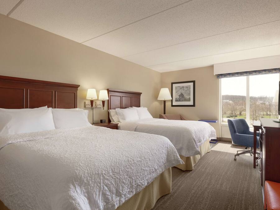 A hotel room with two beds, a desk, a chair, and a television.