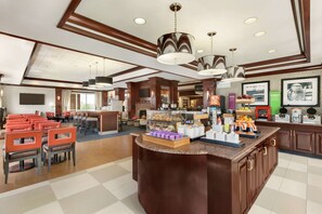 A modern hotel lobby with a central bar area, seating arrangements, and a coffee station.