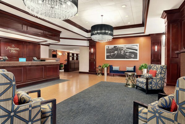 A hotel lobby with a reception desk, seating area, and a large chandelier.