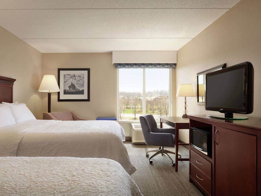 Habitación de hotel con dos camas, un escritorio con televisor, una silla y ventana con vistas.