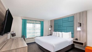 Una habitación de hotel con una cama grande, un escritorio, un televisor y una ventana con cortinas.