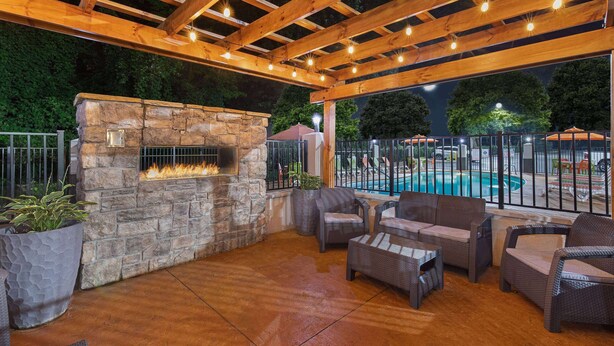 Un patio exterior con paredes de piedra, una chimenea, muebles de mimbre y vista a una piscina.