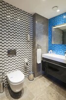 Un baño moderno con pared de azulejos, inodoro, lavamanos y espejo.