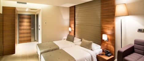 Quarto de hotel com duas camas, uma mesa de cabeceira com telefone, luminária e uma cadeira.