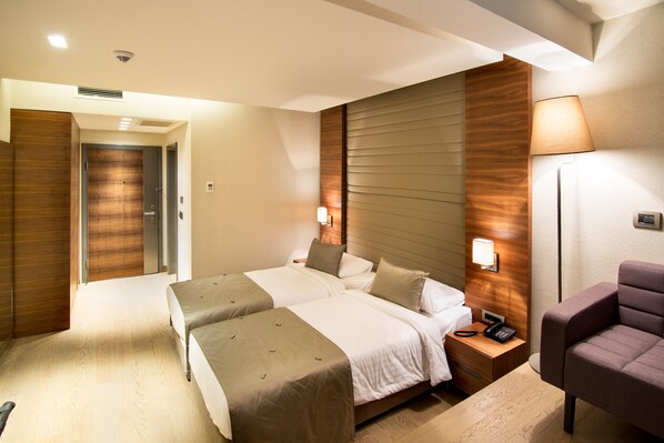 A hotel room with two beds, a nightstand with a phone, a lamp, and a chair. - Hotel Arcadia Blue Istanbul (Istanbul)