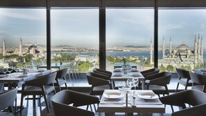 A restaurant with a view of a cityscape and a mosque. Tables are set with wine glasses and plates. - Hotel Arcadia Blue Istanbul (Istanbul)