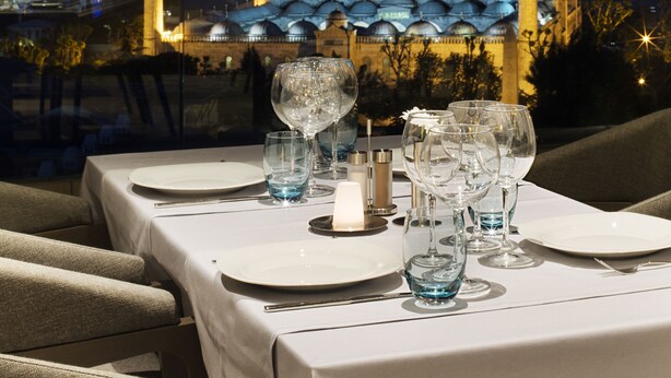 A table set for dining with a view of a mosque with multiple minarets and domes in the background. - Hotel Arcadia Blue Istanbul (Istanbul)