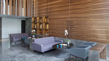 Un vestíbulo moderno con un panel de madera, un área de estar con sofás, una mesita de café y una planta pequeña.