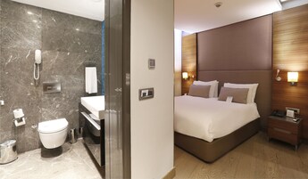 A modern hotel room with a marble bathroom, a separate bedroom with a large bed, and a wooden headboard.