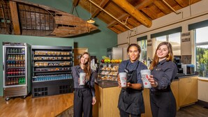 A café interior with wooden beams, a coffee machine, and a refrigerated display case with beverages. - Grande Denali Lodge (Denali National Park)