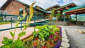 A log cabin hotel with a wooden exterior, a covered outdoor area with stairs, and a flower garden. - Grande Denali Lodge (Denali National Park)