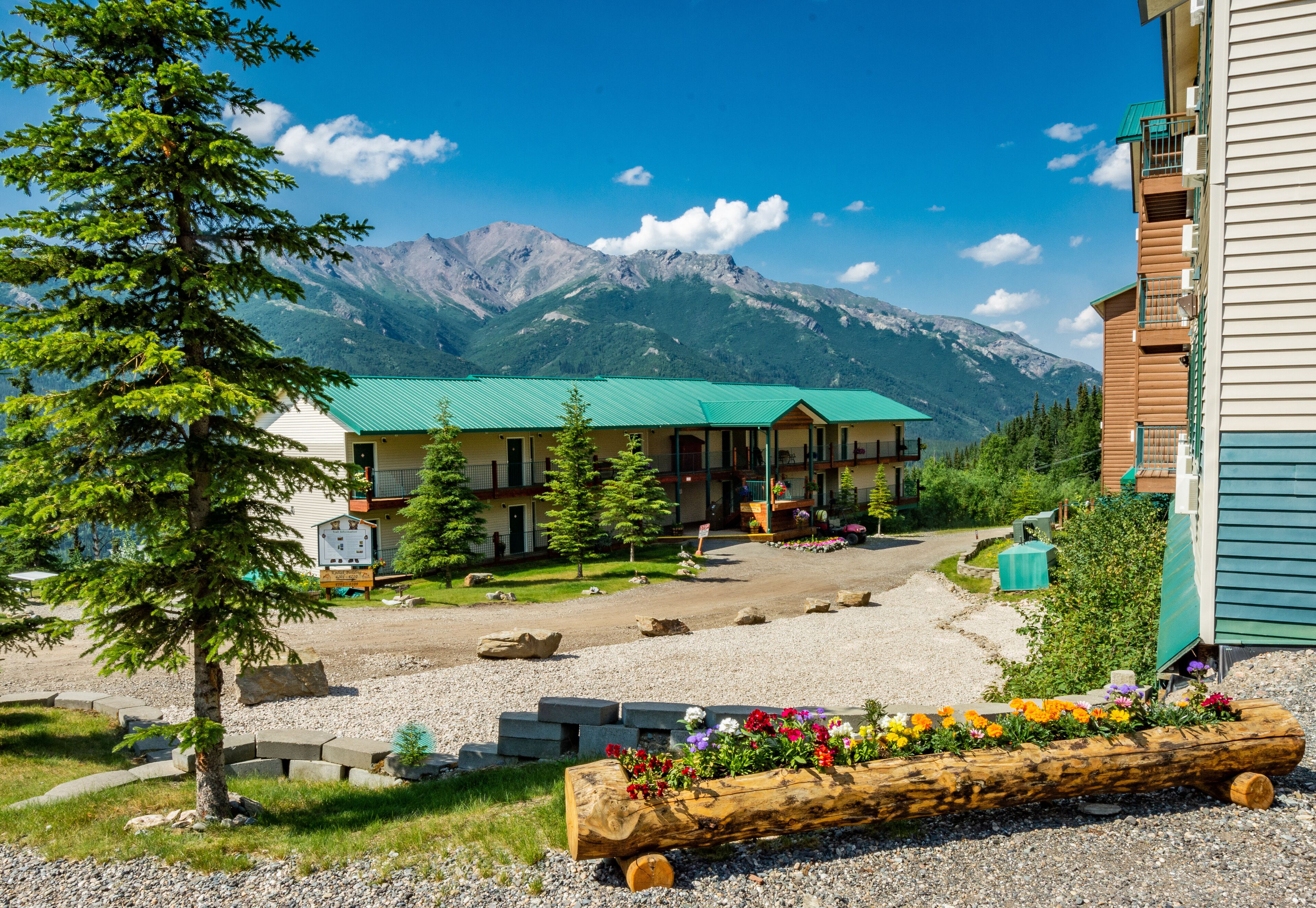 A lodge with a green roof, a gravel driveway, and a mountain backdrop.