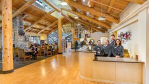 A spacious lobby with wooden beams, a stone fireplace, and a reception desk with staff. - Grande Denali Lodge (Denali National Park)