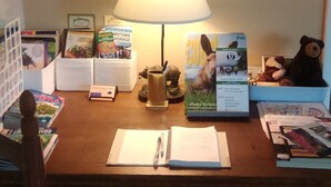 A wooden desk with two wall clocks, a lamp, and various books and magazines. - Alaska European Bed & Breakfast (Anchorage)