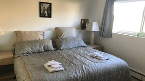 A neatly made bed with a patterned bedspread and pillows, a bedside table with a lamp, and a framed picture on the wall. - Alaska European Bed & Breakfast (Anchorage)