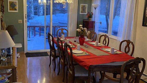 A dining room with a red tablecloth, wooden chairs, and a chandelier. - Alaska European Bed & Breakfast (Anchorage)
