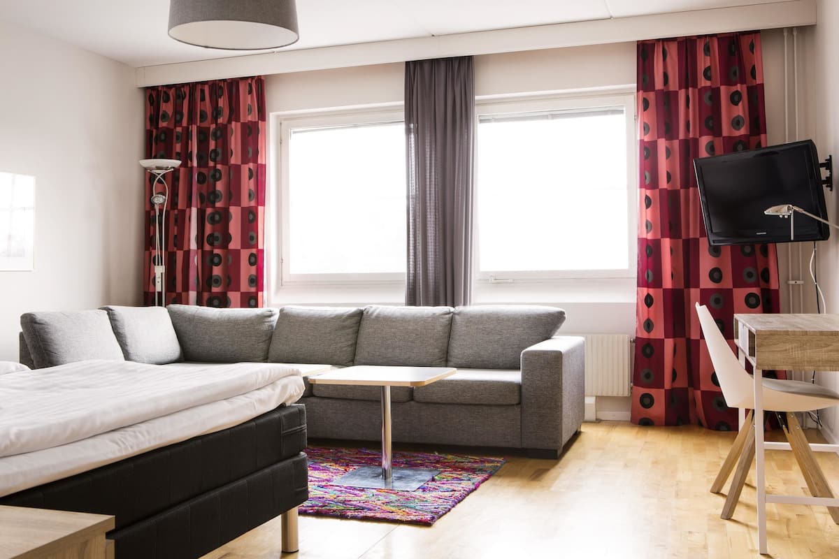 A modern room with a bed, grey sofa, small table, and a TV on a stand.