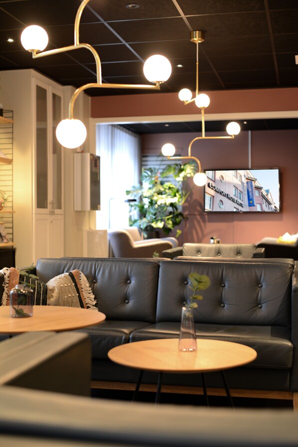 A modern interior with a leather sofa, round tables, and pendant lighting. - Comfort Hotel Arctic (Luleå)